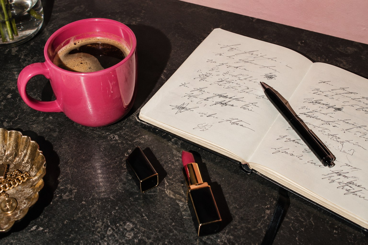 Pink coffee cup, open notebook and lipstick on a dark table